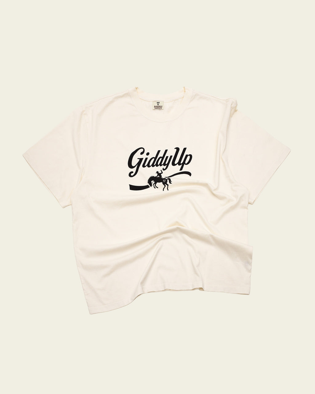 Ayredale Ranch & Co cream cotton t-shirt featuring a black Giddy Up graphic with a bucking horse silhouette.