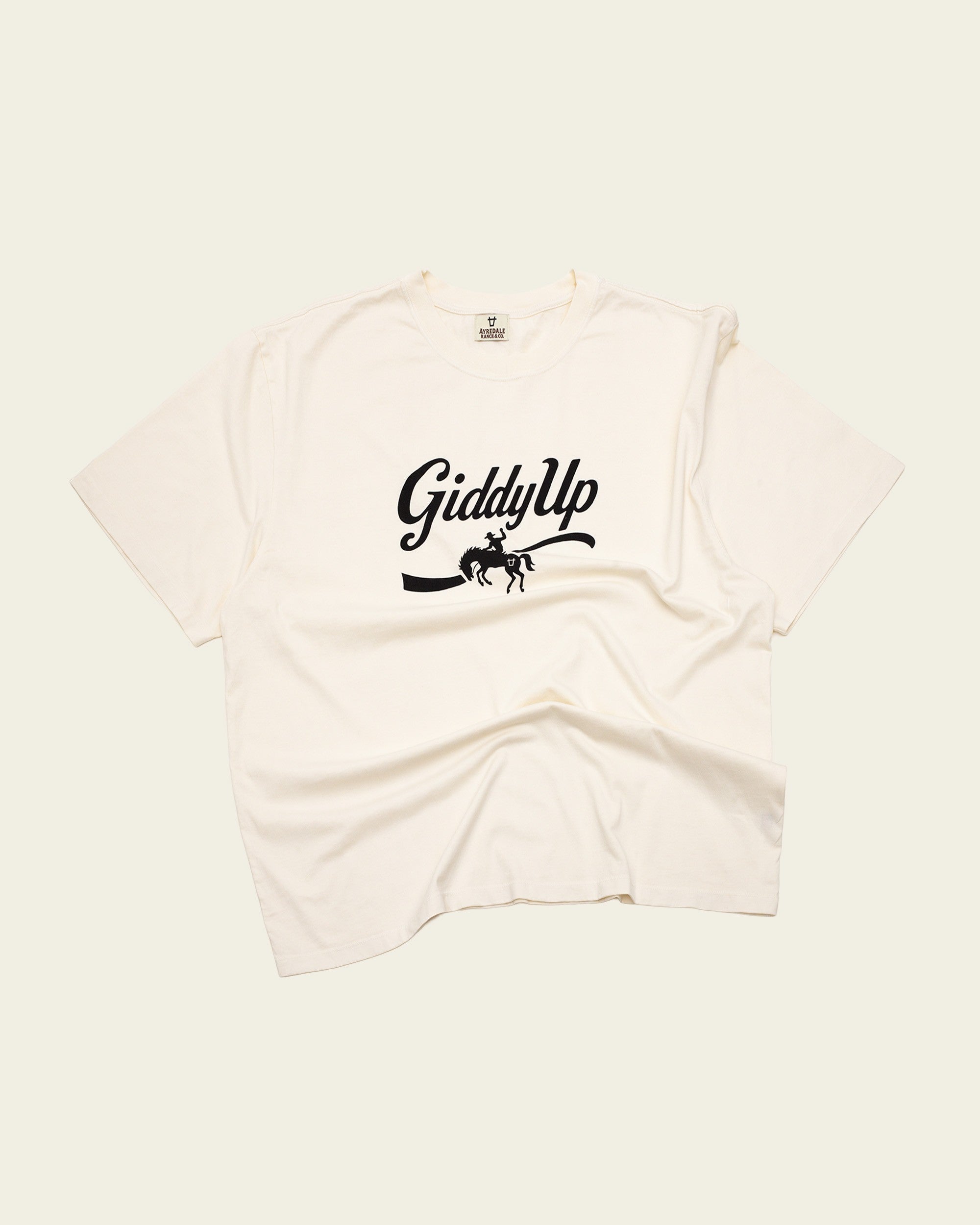 Ayredale Ranch & Co cream cotton t-shirt featuring a black Giddy Up graphic with a bucking horse silhouette.