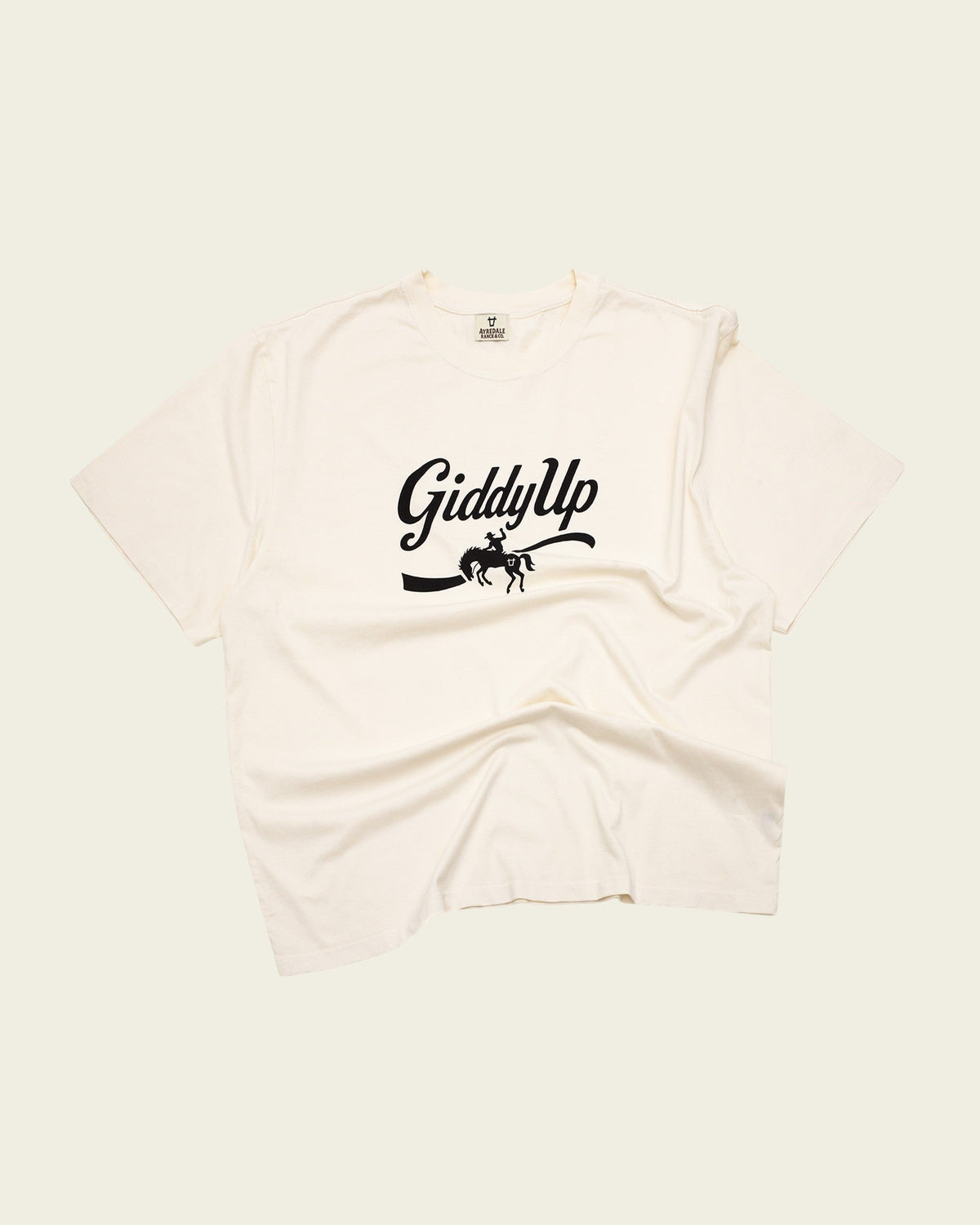 Ayredale Ranch & Co cream cotton t-shirt featuring a black Giddy Up graphic with a bucking horse silhouette.