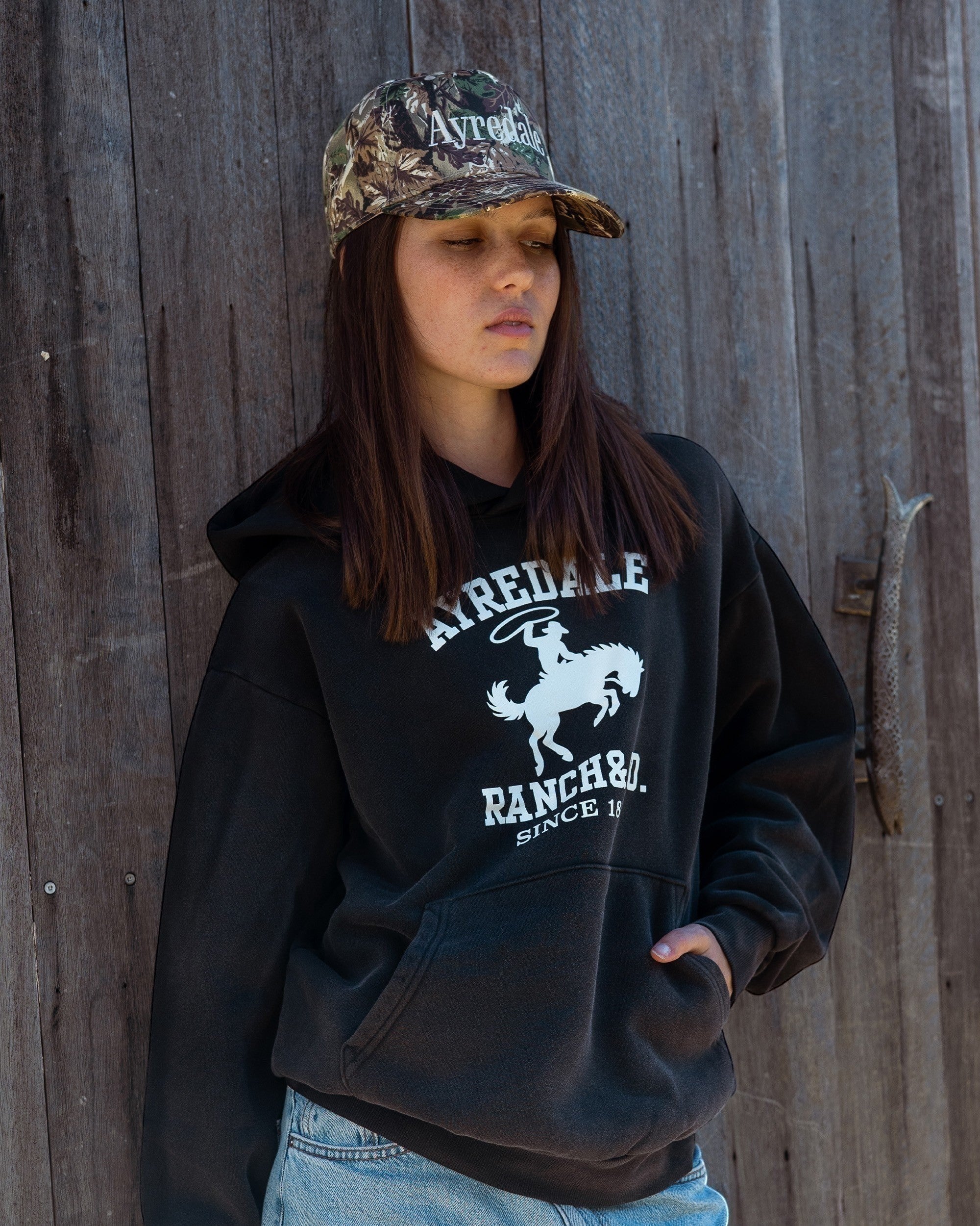 Ayredale Ranch & Co. black heavyweight fleece hoodie with collegiate graphic and kangaroo pocket, worn by a woman.