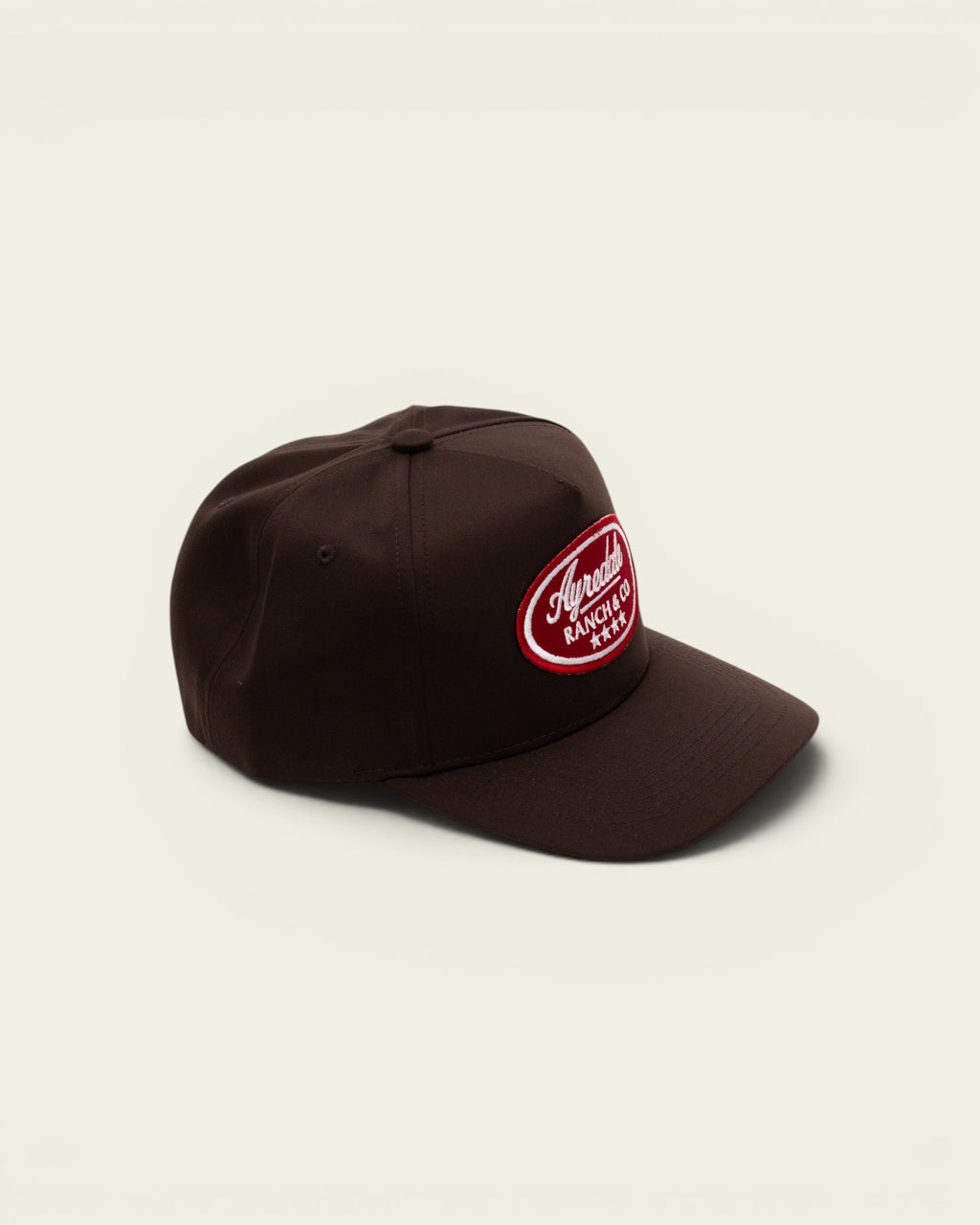 Ayredale Ranch & Co dark brown baseball cap with a red oval patch featuring white embroidered logo text
