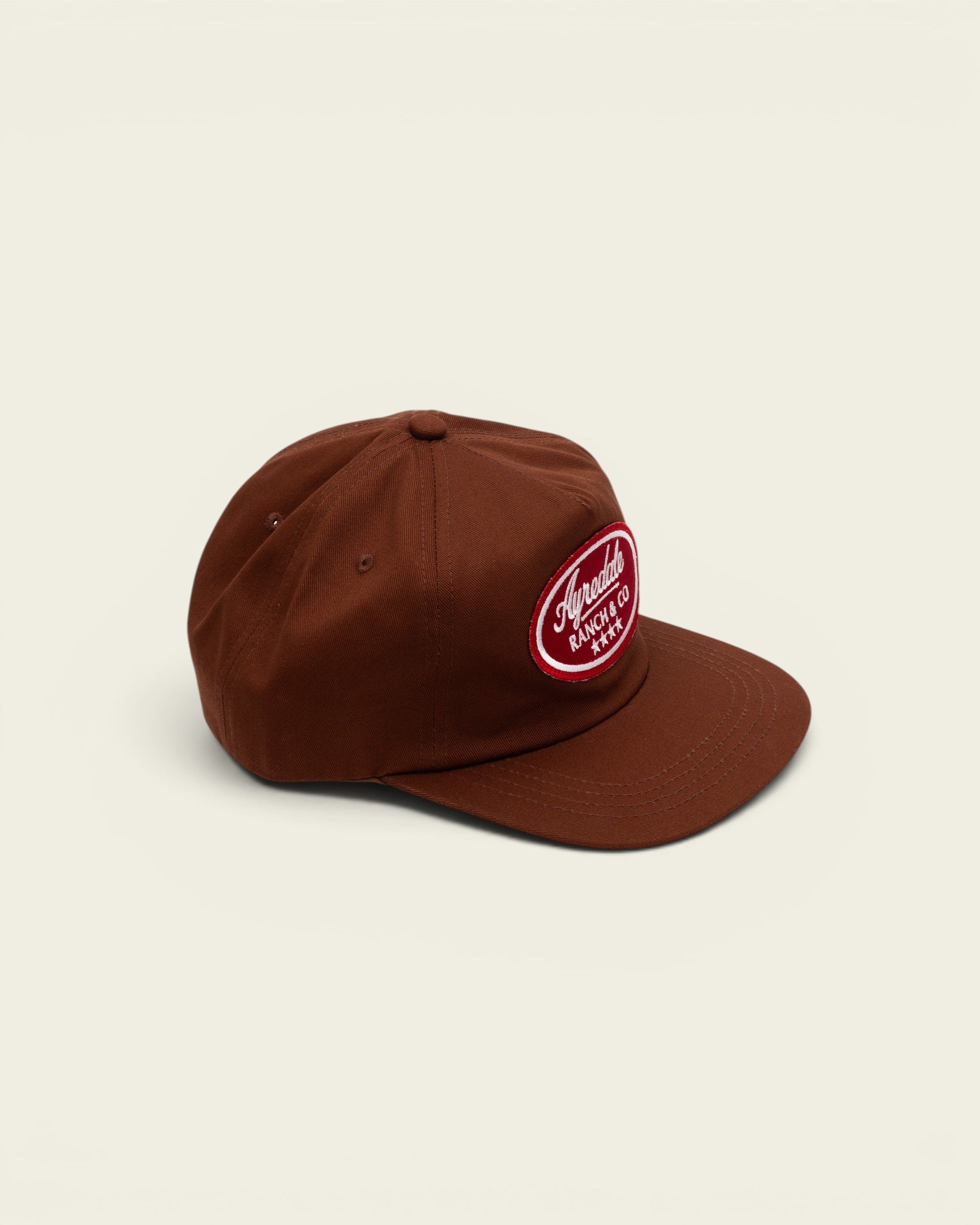 Ayredale Ranch & Co brown baseball cap featuring a red oval patch with white embroidered logo and four stars.