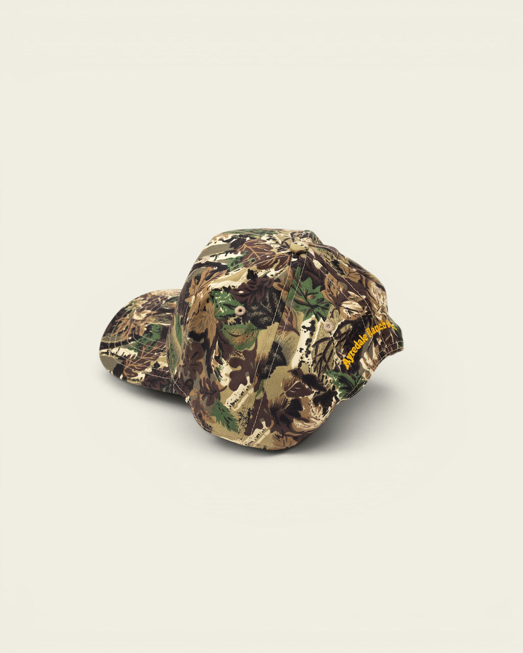 Ayredale Ranch & Co camouflage baseball cap with yellow embroidered logo on the side.