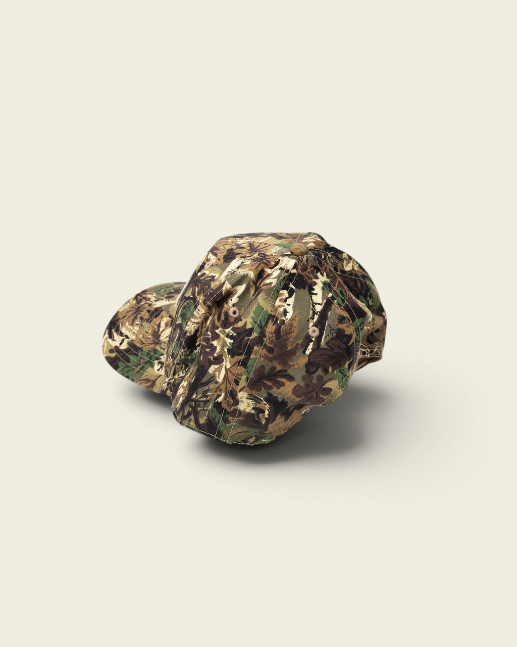 Ayredale Ranch & Co camouflage baseball cap with green, brown, and tan woodland pattern. Features a button top and stitched details.