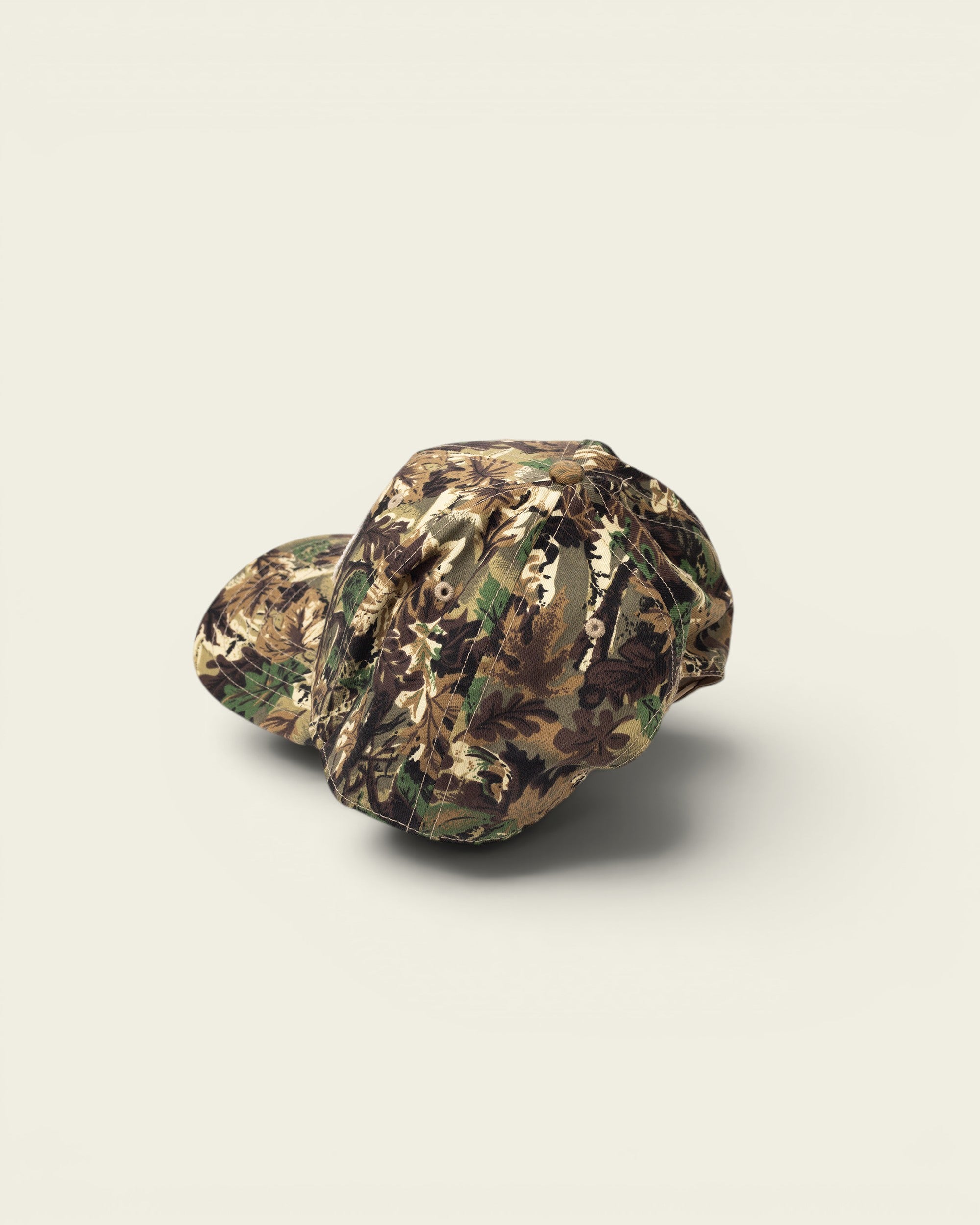 Ayredale Ranch & Co camouflage baseball cap with green, brown, and tan woodland pattern. Features a button top and stitched details.