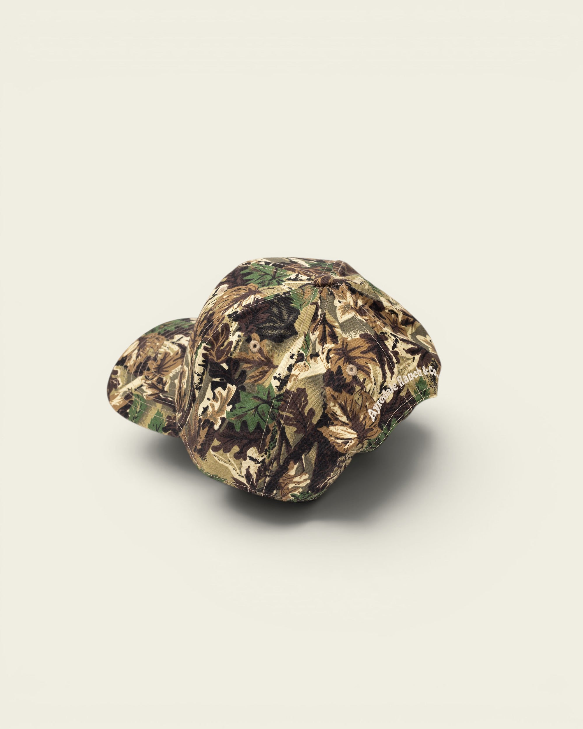 Ayredale Ranch & Co camouflage baseball cap with leaf pattern in green, brown, and tan.