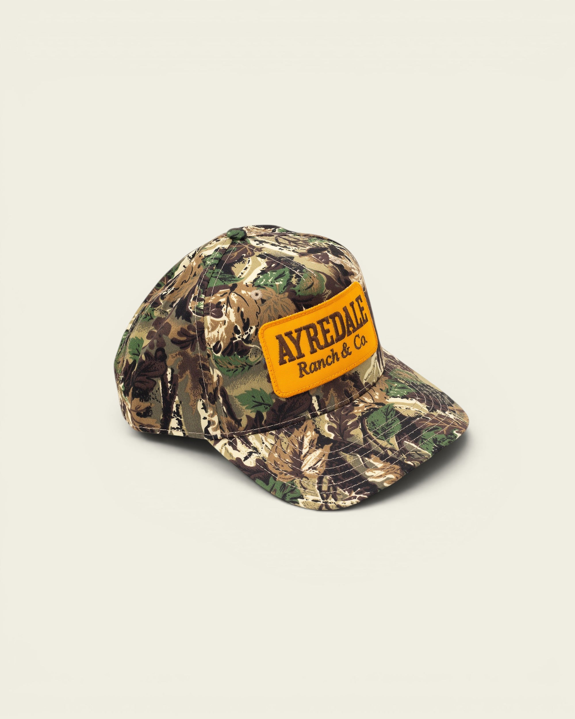 Ayredale Ranch & Co camouflage baseball cap with orange patch logo.