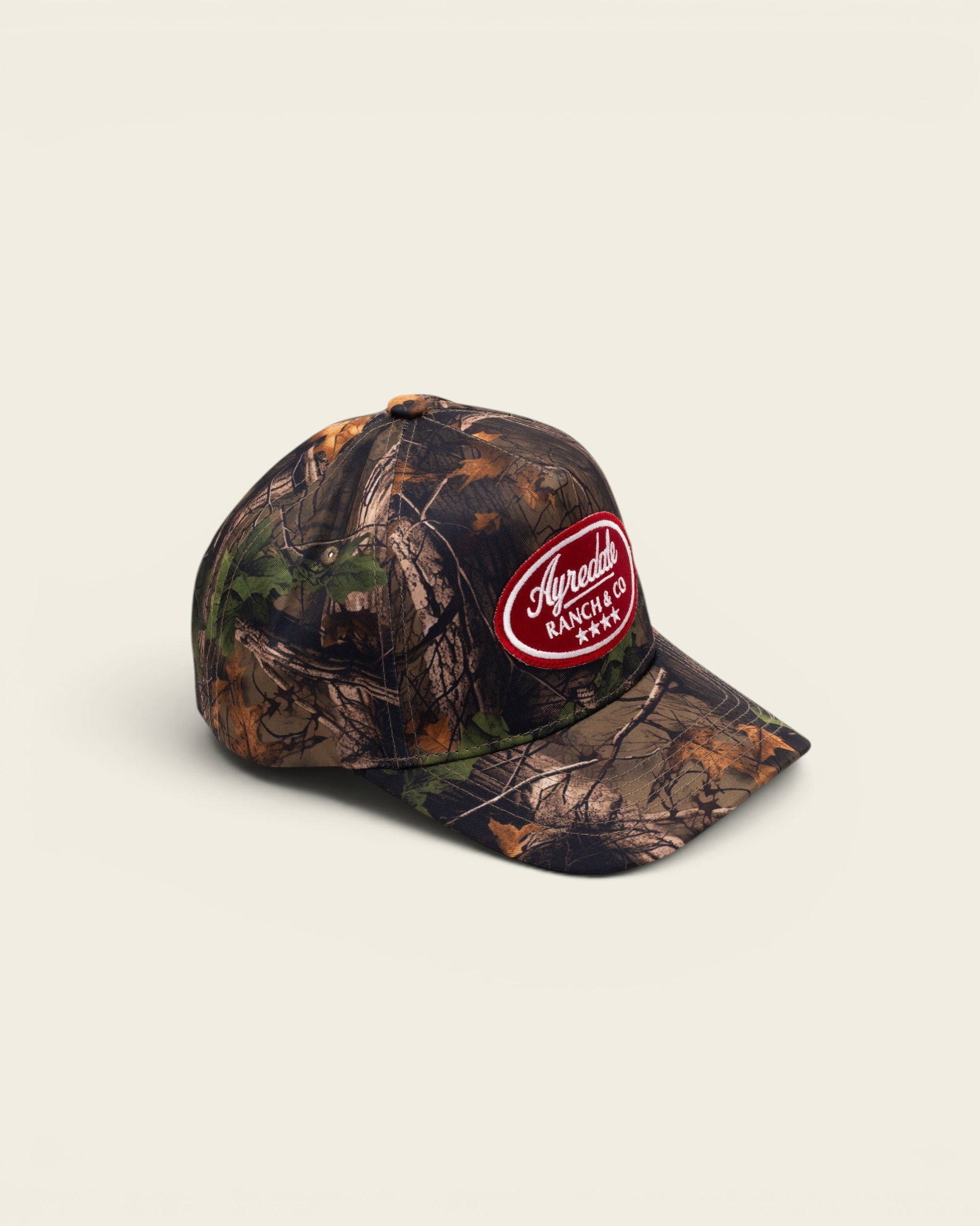 Ayredale Ranch & Co camo baseball cap with a red oval patch logo and four white stars on a white background