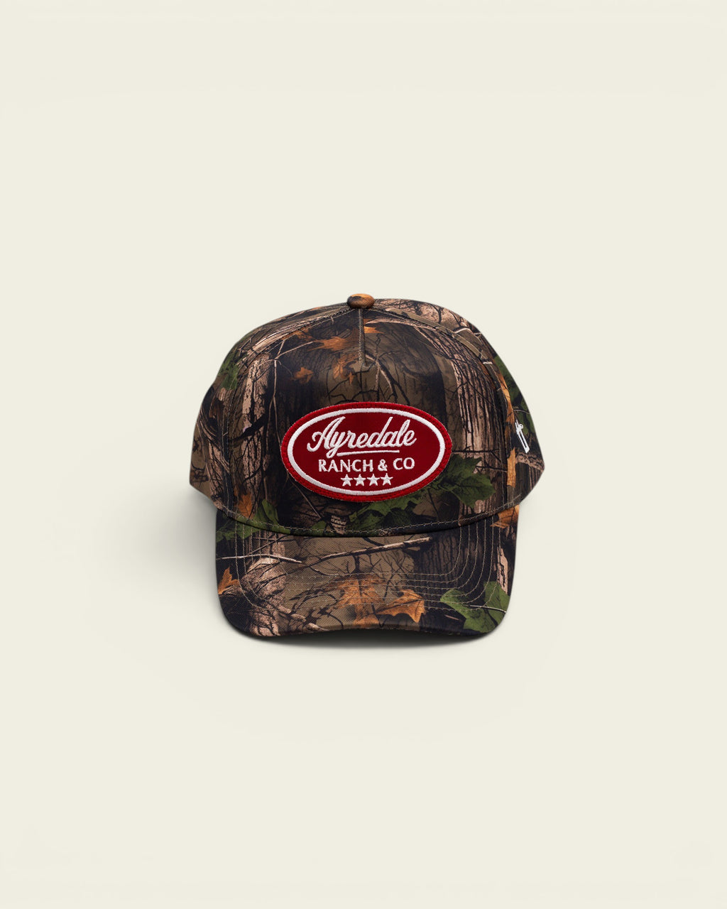 Ayredale Ranch & Co baseball cap featuring a forest camouflage pattern and a red oval patch with white logo text.