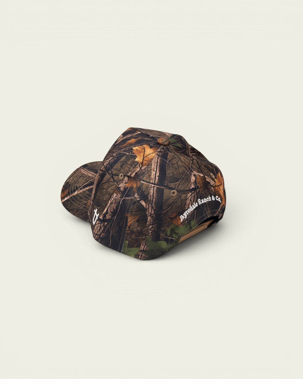 Ayredale Ranch & Co. camouflage baseball cap with a realistic tree bark and leaf pattern. Features embroidered logo on the side.
