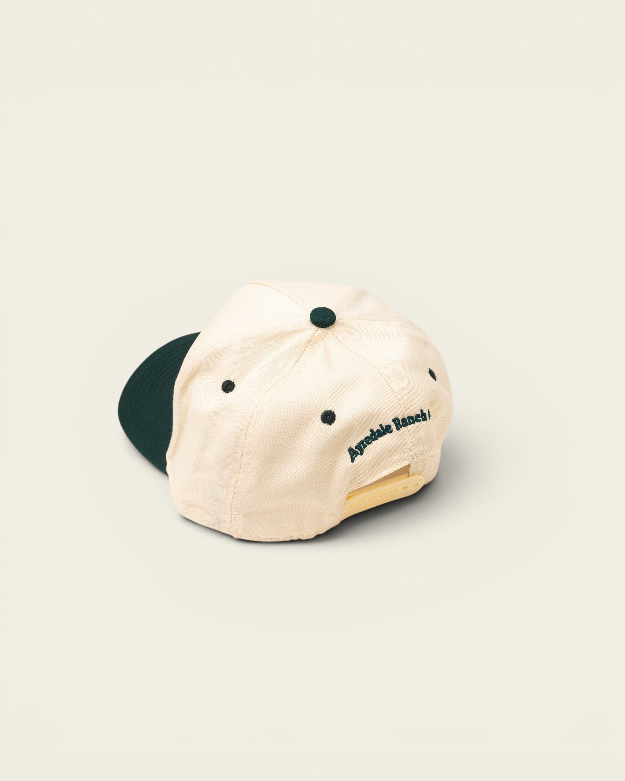 Ayredale Ranch & Co cream baseball cap with dark green brim and embroidered logo on back.