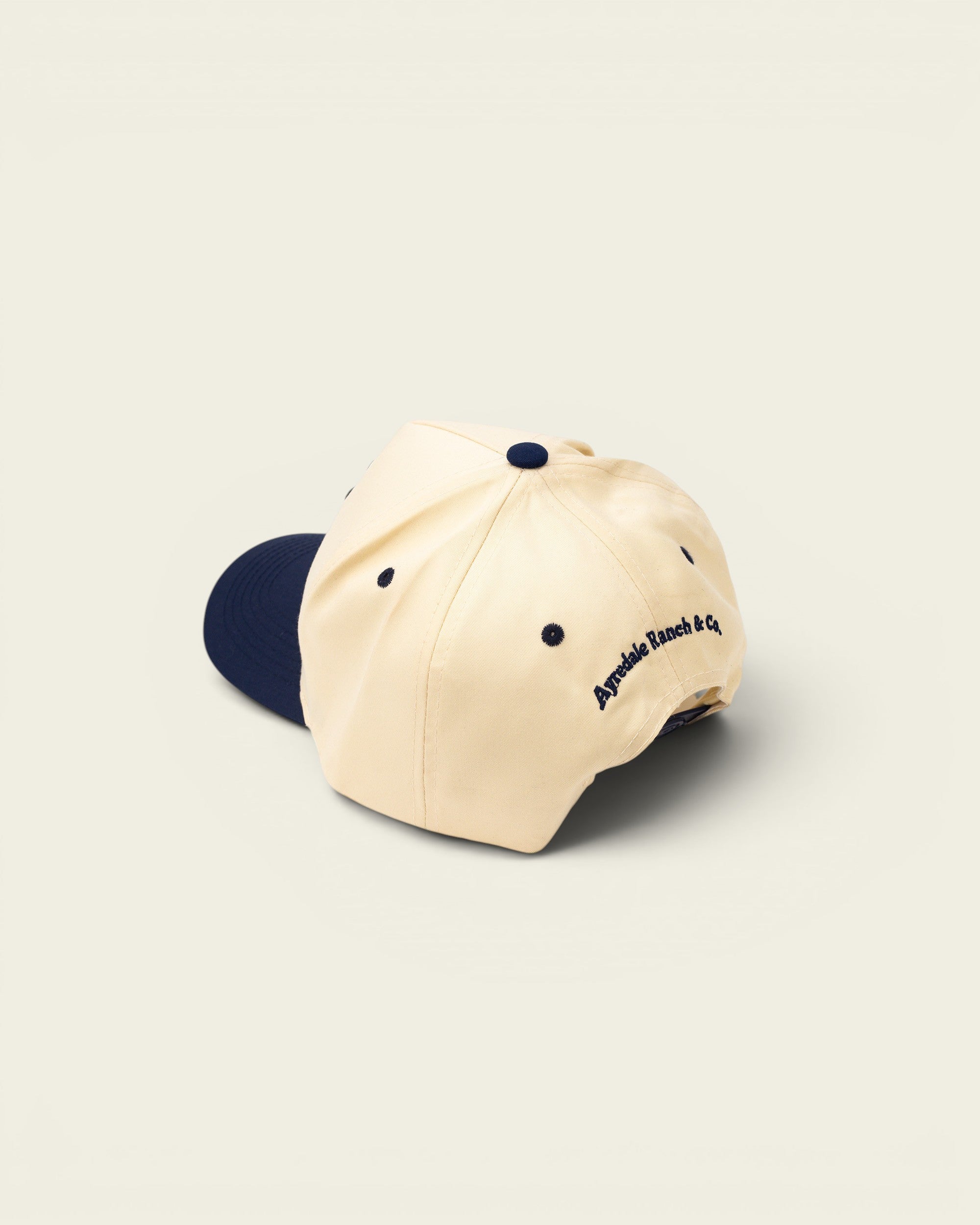 Ayredale Ranch & Co cream baseball cap with navy blue brim and embroidered logo
