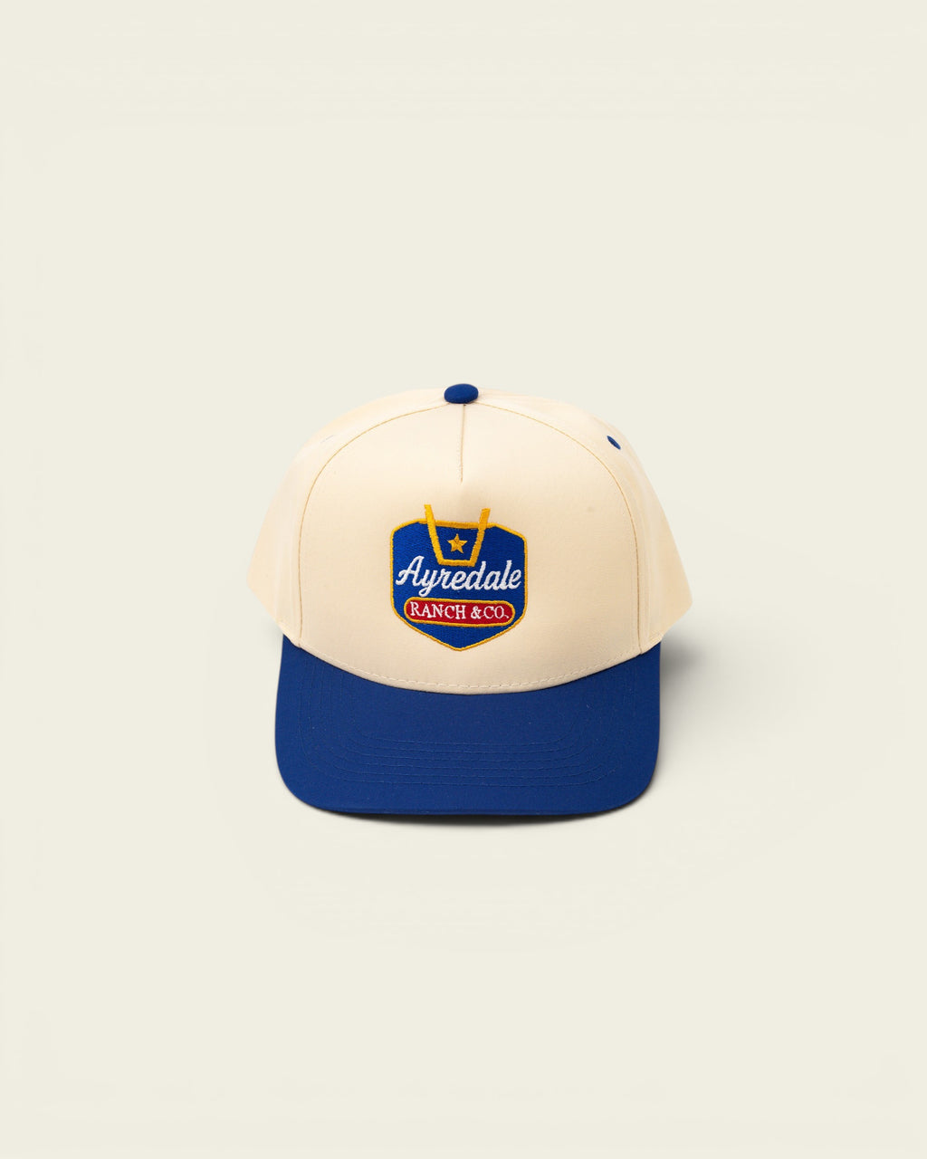 Ayredale Ranch & Co cream baseball cap with blue brim and embroidered logo.