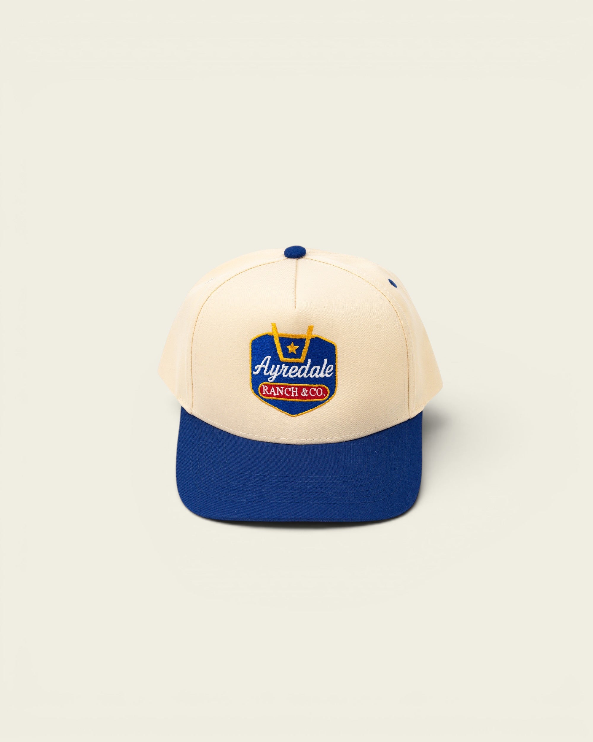 Ayredale Ranch & Co cream baseball cap with blue brim and embroidered logo.