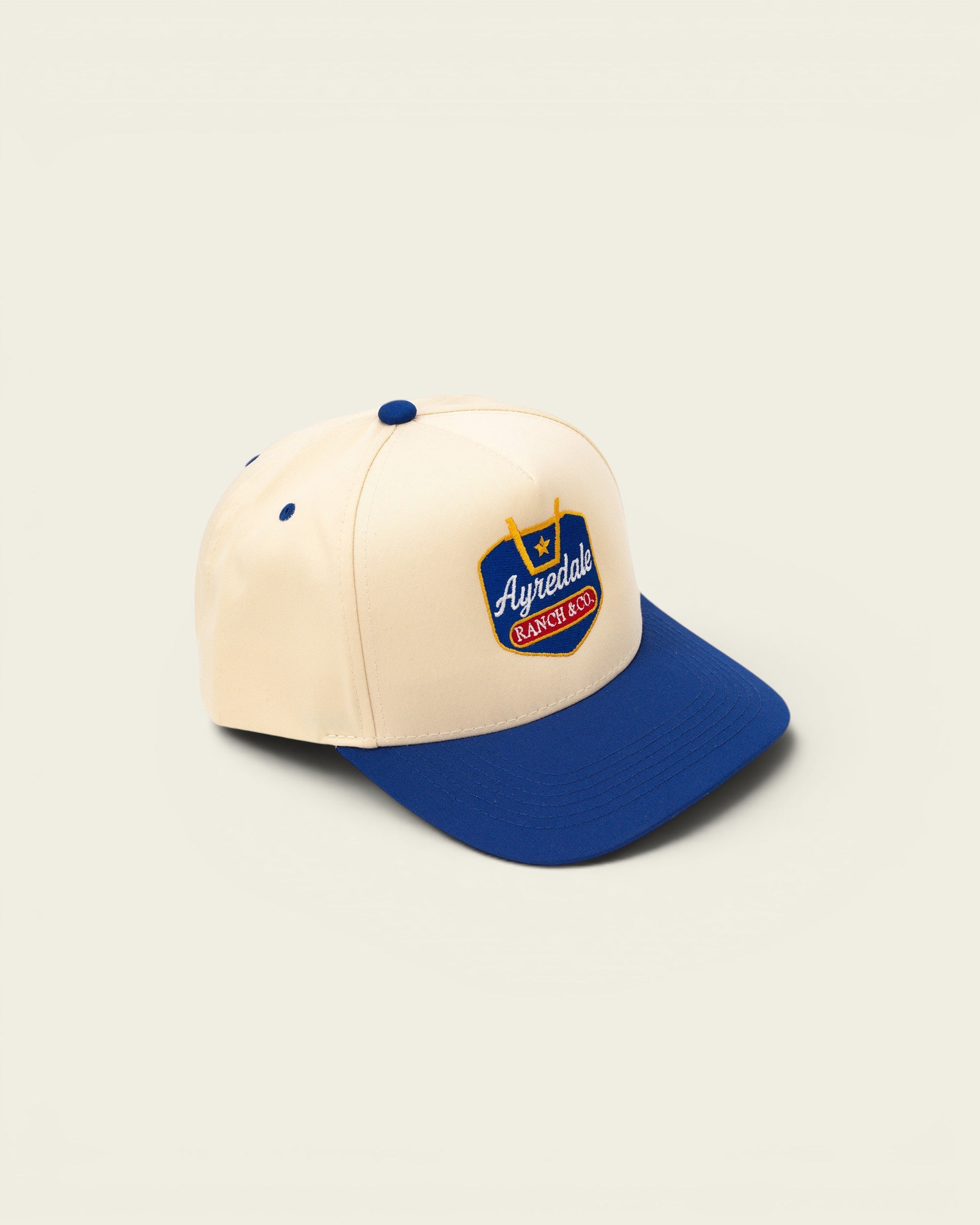 Ayredale Ranch & Co cream baseball cap with blue brim and embroidered logo.