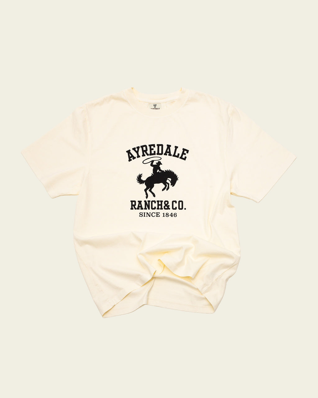 Ayredale Ranch & Co cream cotton t-shirt featuring a black graphic of a cowboy on a bucking horse