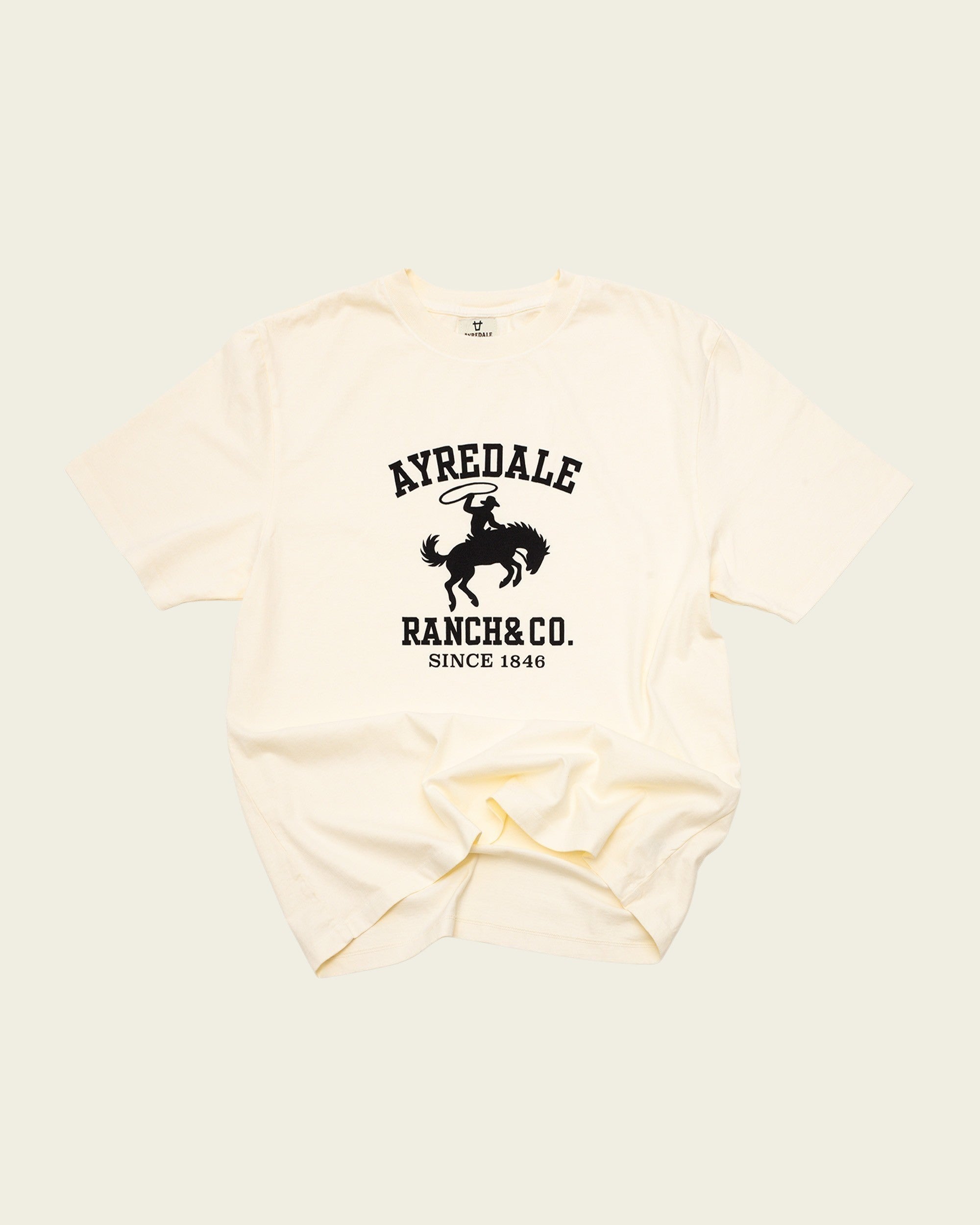 Ayredale Ranch & Co cream cotton t-shirt featuring a black graphic of a cowboy on a bucking horse