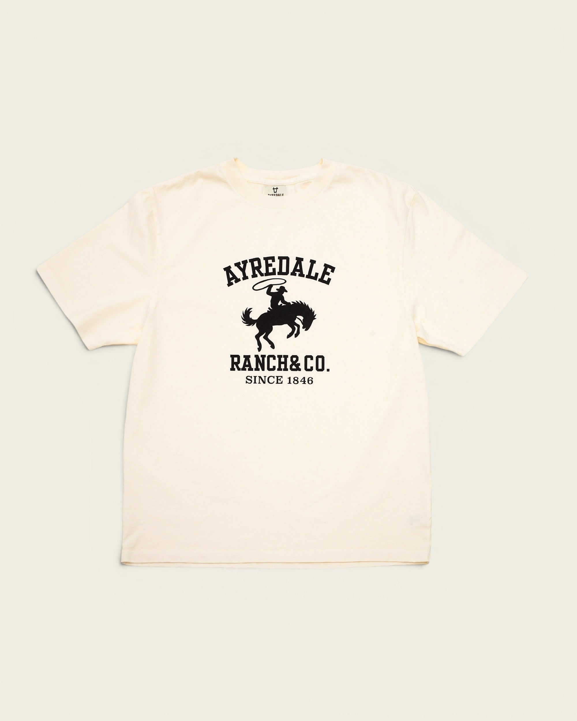 Ayredale Ranch & Co cream cotton t-shirt featuring a black graphic of a cowboy riding a bucking horse.