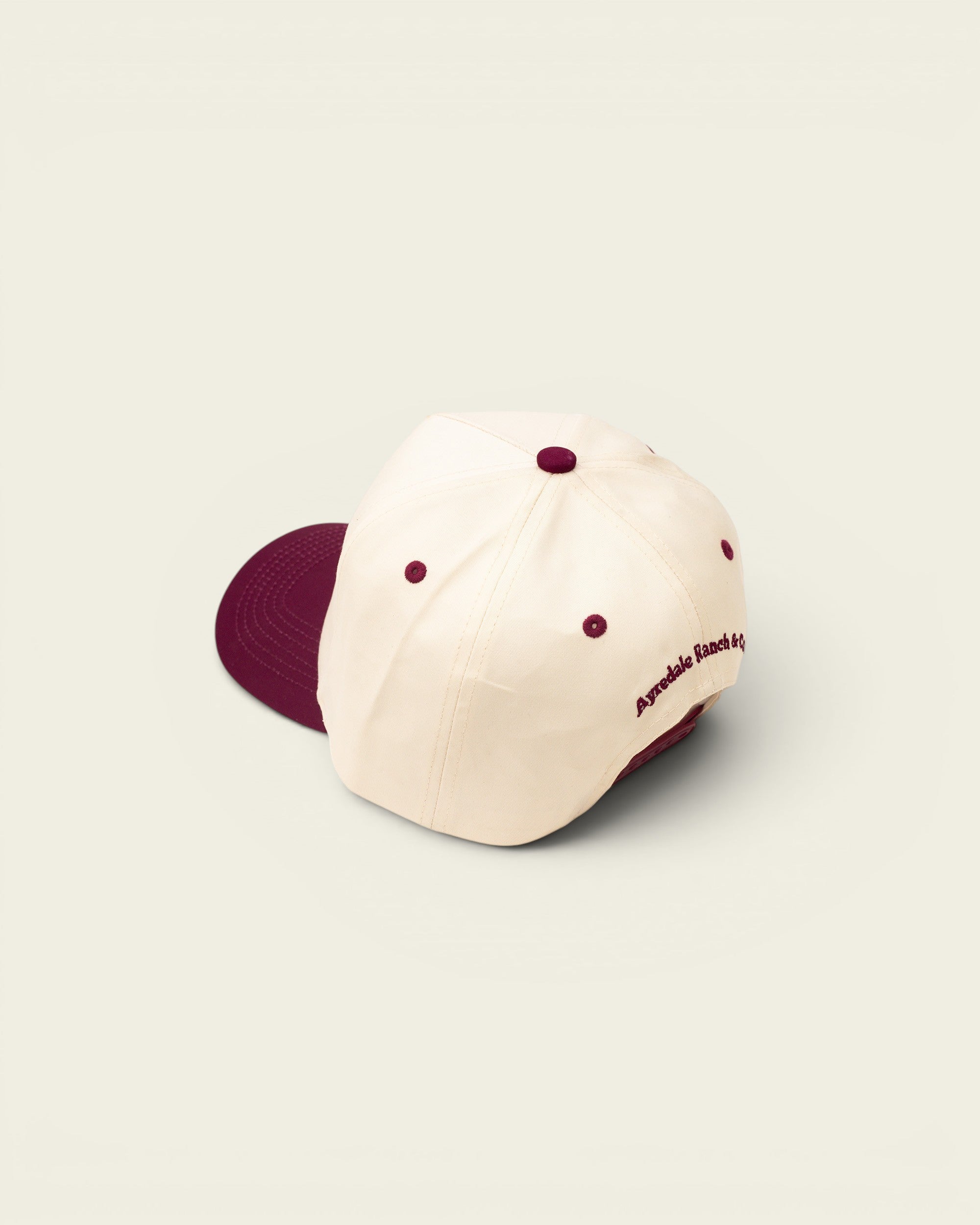 Ayredale Ranch & Co cream baseball cap with maroon accents and embroidered logo on the side.