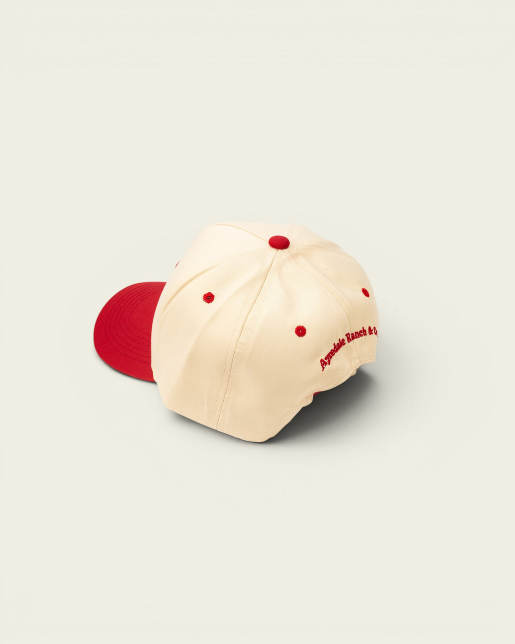 Ayredale Ranch & Co cream baseball cap with red button and embroidery detail.