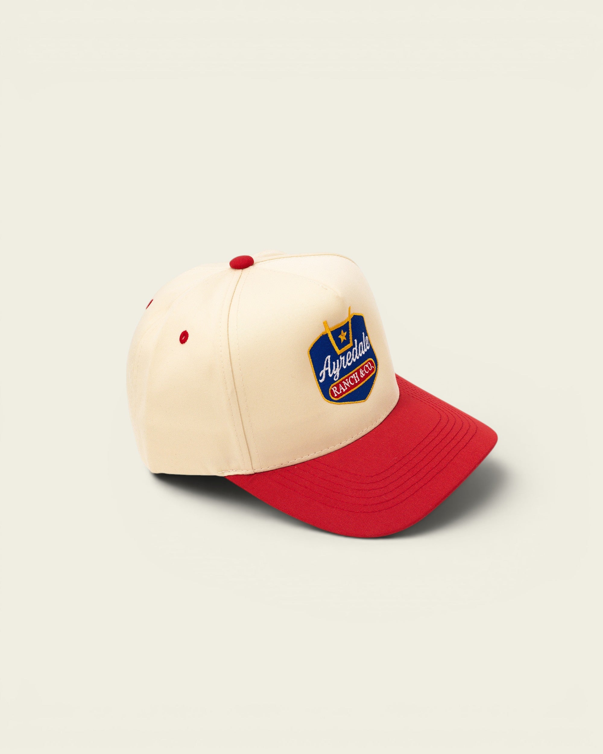 Ayredale Ranch & Co cream baseball cap with red brim and embroidered logo.