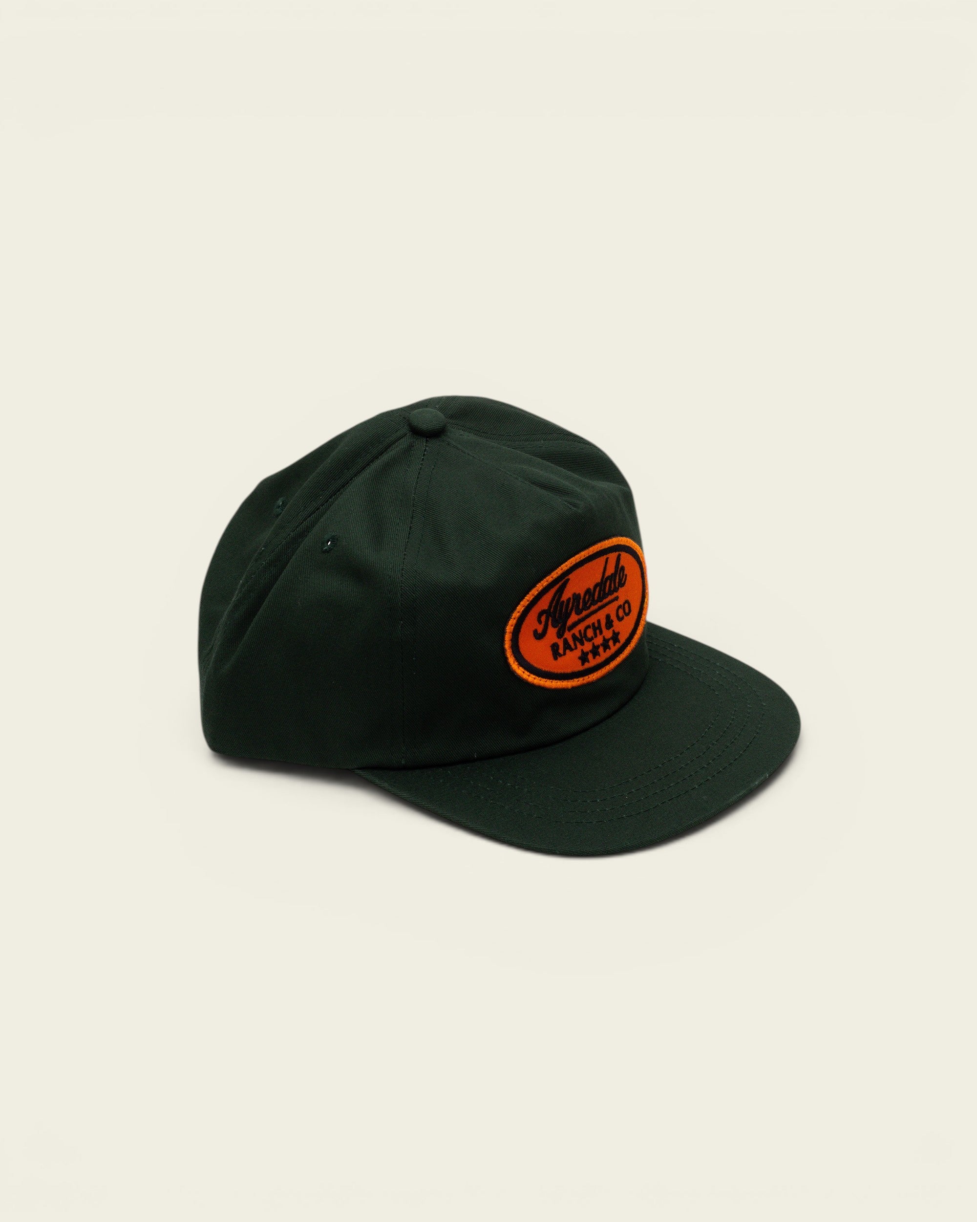 Ayredale Ranch & Co dark green baseball cap with an oval orange patch featuring black embroidered text and stars.